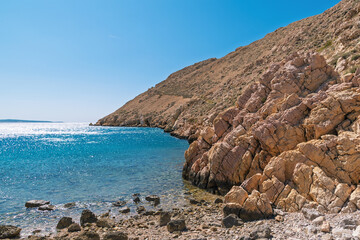 Sunny rocky coastline with clear blue sea and rugged hills