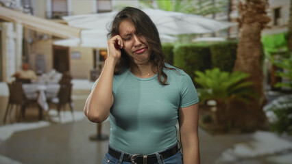 Fototapeta premium Woman with hands covering face on a street terrace restaurant, eyes closed and shoulders tense; sadness.
