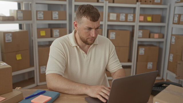 Man typing on laptop and jotting on a sticky note amid cardboard parcels on shelves in a building; focused productivity.