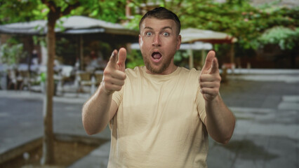 Naklejka premium Man raising clenched fists with bare forearms and open mouth cheering on a sunny street cafe terrace with umbrellas and trees; victory joy.