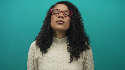 Woman in cableknit sweater tilts head back with closed eyes in a studio against a teal wall;...