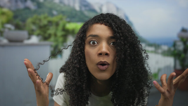 African american woman raises hands to head in forest with wide eyes and open mouth overlooking mountains; surprise.