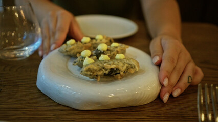 Woman hands framing a plate of fried bites topped with yellow dollops on a marble platter in a building; quiet anticipation.