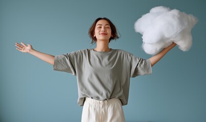 Young woman smiling joyfully with a cloud prop in a studio against a blue background, demonstrating creativity and playfulness