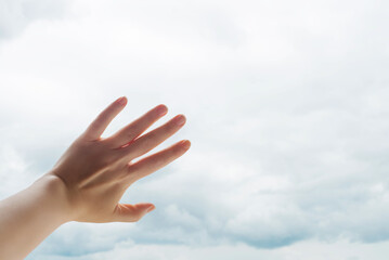 Female hand reaching toward bright cloudy sky, symbolizing hope, freedom, letting go and new beginnings