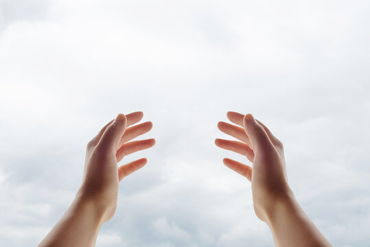 Female hands lifted toward the sky in a gesture of faith, prayer, hope, and spiritual connection against a soft cloudy background