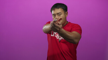 Young chinese lifeguard man gestures finger to lips for silence in pink studio with whistle around...