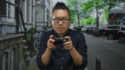 Young chinese man gripping a game controller with tense hands on a busy street; competitive frustration.