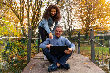 Mature couple interacting with a laptop while relaxing outdoors on a bridge