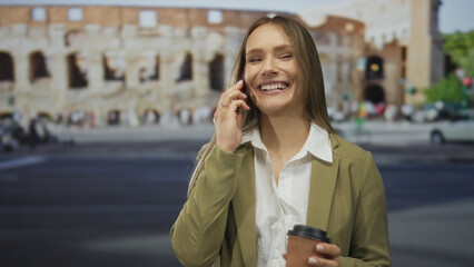 Woman talking on smartphone while holding coffee in front of roman coliseum in outdoor city setting, showcasing urban life and travel.