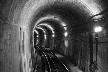 モノクロームで表現されたコンクリートでできた暗く丸いトンネルの奥へと続く線路と照明の光を捉えた交通手段の風景