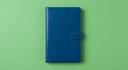 A closed blue leather-bound notebook with a strap closure placed on a pastel green background for writing or note-taking purposes
