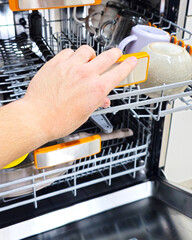 Person closing the top rack of a modern dishwasher filled with clean cups and plates, representing household chores, cleanliness, hygiene, and daily home care in a contemporary kitchen.