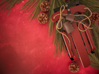 Background for personalized Christmas card. Overhead red texture background with holiday wood sled, weathered rustic metal bells and jute twine, long pine branches and needles, and festive pinecones. 
