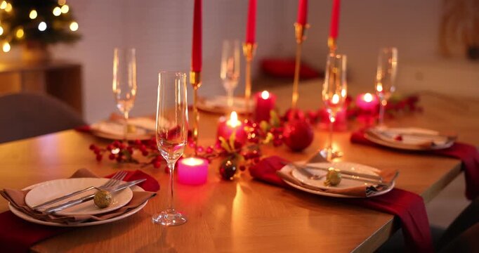 Stylish Christmas table setting with plates, glasses and burning candles in festive decorated room, closeup. Camera moving in