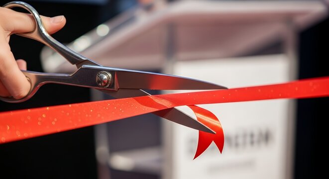 Person Cutting Red Ribbon with Scissors at Ribbon Cutting Ceremony