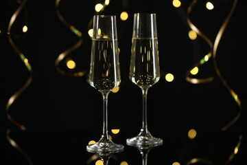 New Year celebration. Sparkling wine in flute glasses and serpentine streamers on black background, bokeh lights