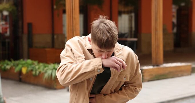 Young man eating bun and suffering from nausea outdoors