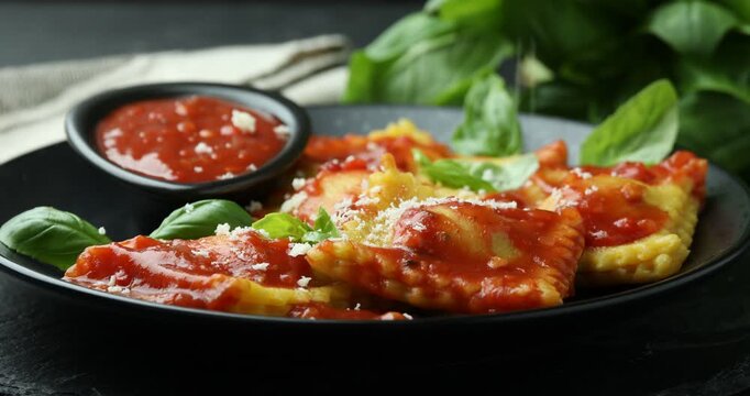 Adding parmesan cheese onto delicious ravioli with tomato sauce and basil at table, closeup