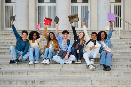 Group of diverse students feeling happy and celebrating success, raising books on university stairs