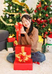 Asian young beautiful woman sitting on carpet floor wearing reindeer antlers pose smile with red gift box presents ornaments decorated in living room Merry christmas happy new year festival celebrated