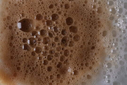 ​Coffee Foam Texture: Close-up macro shot of brown and white microfoam bubbles on a cappuccino or latte.
