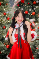 young asian woman in a red santa dress posing among decorated christmas trees with warm festive lights and red ornaments, captured with soft bokeh for holiday-themed