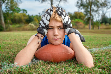 Young male football player lying on a grassy field alone and exhausted gathering his thoughts before the next practice drill