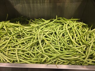 A large quantity of fresh green beans, loosely piled in a metal display bin.