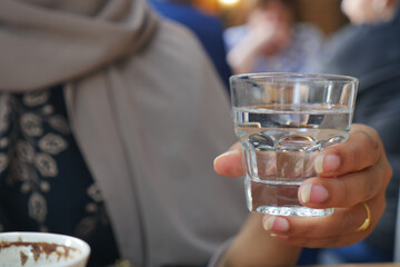 Hand holding a clear glass of water in a cafe setting