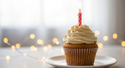 Single cupcake with lit candle, creamy frosting, string lights in background