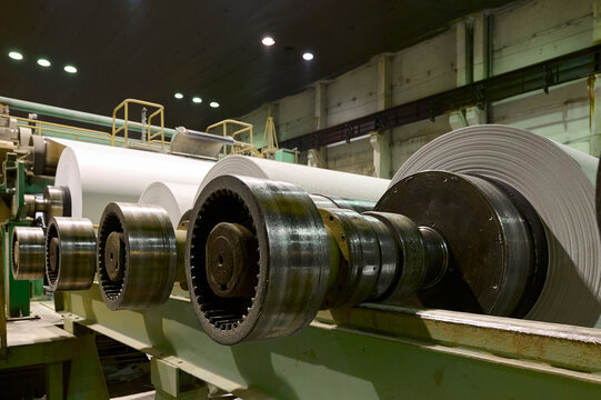 Production process at a paper manufacturing plant showing machinery and large rolls of paper in operation
