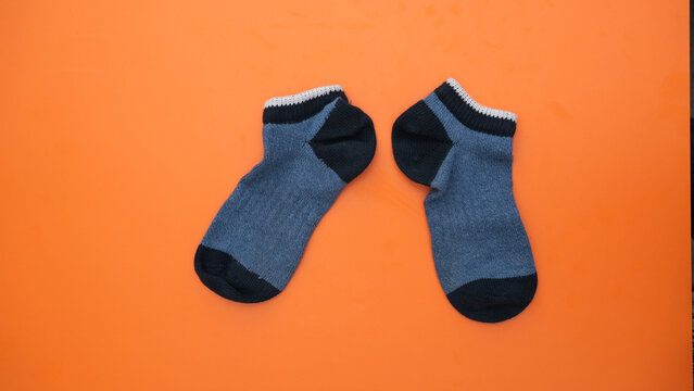 A perfectly matched pair of blue and black ankle socks against a vibrant orange studio background.