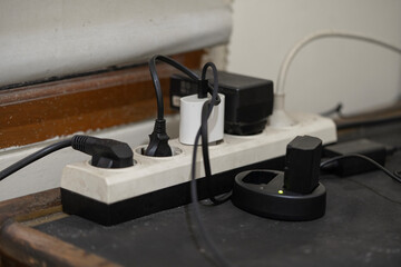 Overloaded power strip with multiple plugs and chargers. A camera battery is charging, shown by the green light.