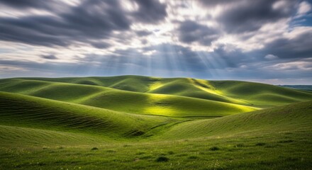Obraz premium Sunlight breaks through dramatic clouds, illuminating rolling green hills with vibrant light and shadow.