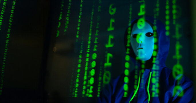 Masked hacker hacking computer. anonymous hacker wearing mask and black hoodie in dark room. online scam and cyber security threat.