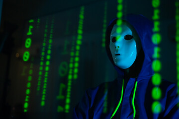 Masked hacker hacking computer. anonymous hacker wearing mask and black hoodie in dark room. online scam and cyber security threat.