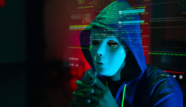 Masked hacker hacking computer. anonymous hacker wearing mask and black hoodie in dark room. online scam and cyber security threat.