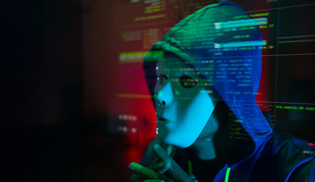 Masked hacker hacking computer. anonymous hacker wearing mask and black hoodie in dark room. online scam and cyber security threat.