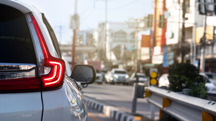 Rear side of luxury white car with trun on brake light. Stop on the junction from traffic light control. Opposite raod with many cars queue up. Blurred of town at day time.