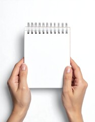 Obraz premium Person holding a small, blank, spiral-bound notepad over white background