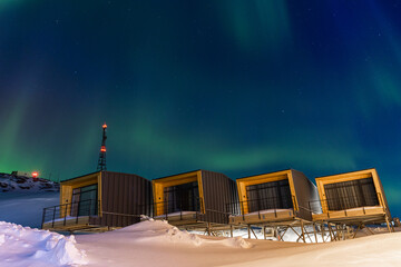 Four modern glamping cabins on raised platforms sit in deep snow under the beautiful teal and green...