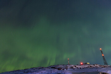 Wide-angle view of the deep green Aurora Borealis lighting up the starry night sky above communication towers on a snow-covered hill