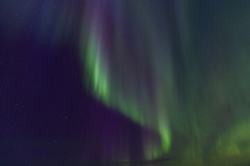 Curtains of green light and magenta hues merge in the vertical display of the Northern Lights, highlighting the densely scattered stars in the dark sky