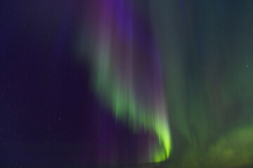 Curtains of green light and magenta hues merge in the vertical display of the Northern Lights, highlighting the densely scattered stars in the dark sky