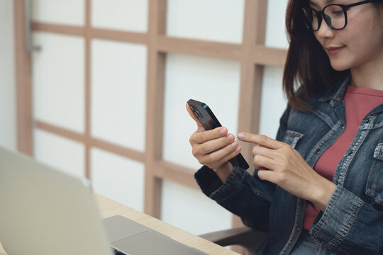 Business woman using smartphone during working on laptop computer at home office. Asian businesswoman, in business casual clothes using mobile phone, surfing the internet, social network - Powered by Adobe