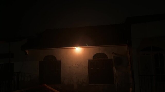 A single light from a house lamp penetrated the enveloping darkness, highlighting the building at night.