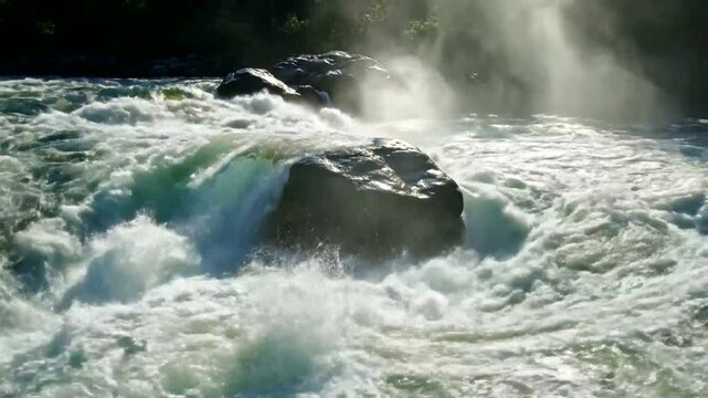 Powerful, churning waterfall cascades over dark, wet rocks with mist rising