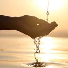 Silhouette of a hand catching water droplets cascading from above, with a golden sunset background over the water