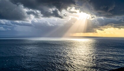 Dramatic seascape captures sun rays breaking through stormy clouds, illuminating the ocean below with a golden glow